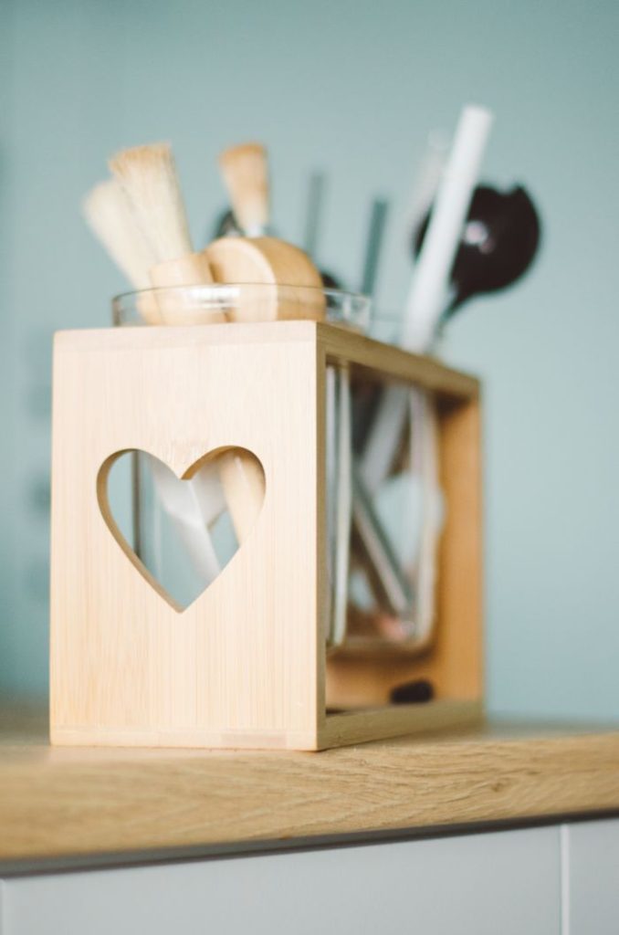 clear-glass-organizer-1635908 Close-up of a wooden utensil holder with a heart cutout, perfect for kitchen decor.