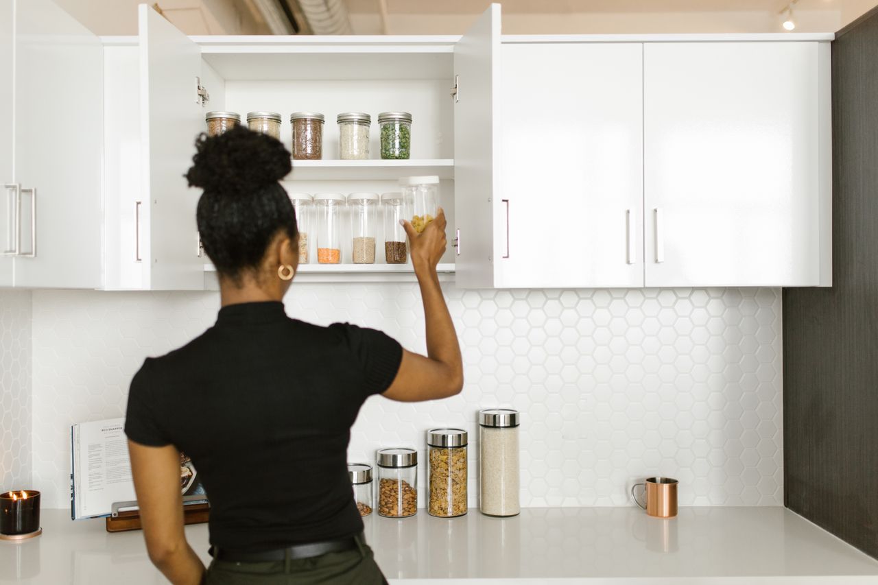 bedroom-bliss A woman organizing a pantry shelf with various food jars in a modern kitchen.